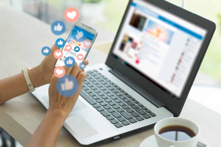 Person using smartphone with social media icons by laptop