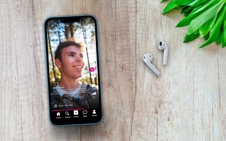 Smartphone showing hiker video beside wireless earbuds