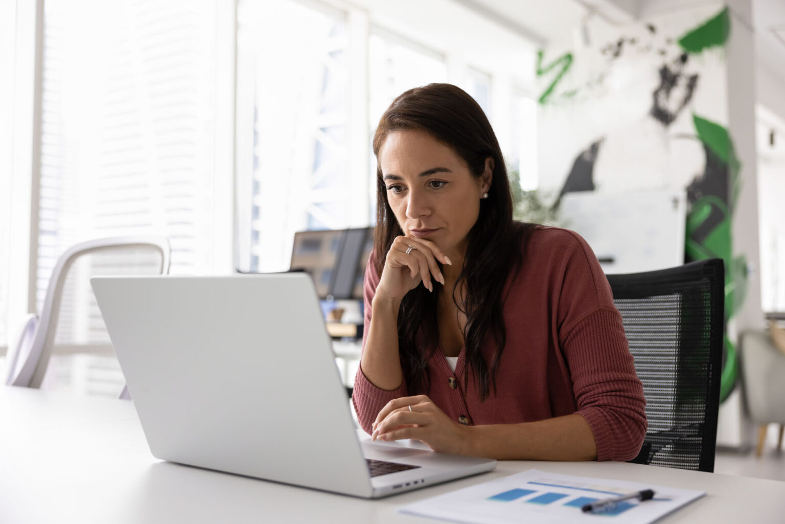 Woman working thoughtfully on laptop in modern office