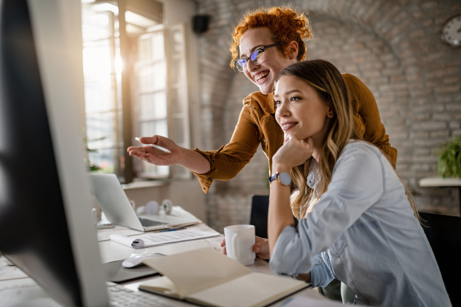 Two colleagues smiling at computer in office