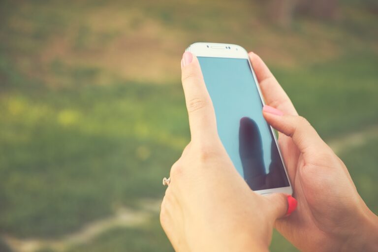 Hands holding smartphone outdoors with blurred background