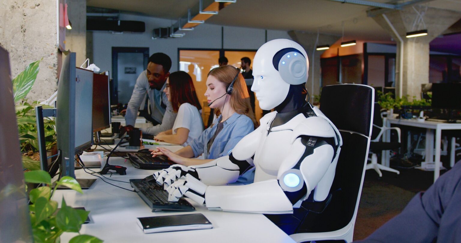 Humanoid robot working at computer in modern office
