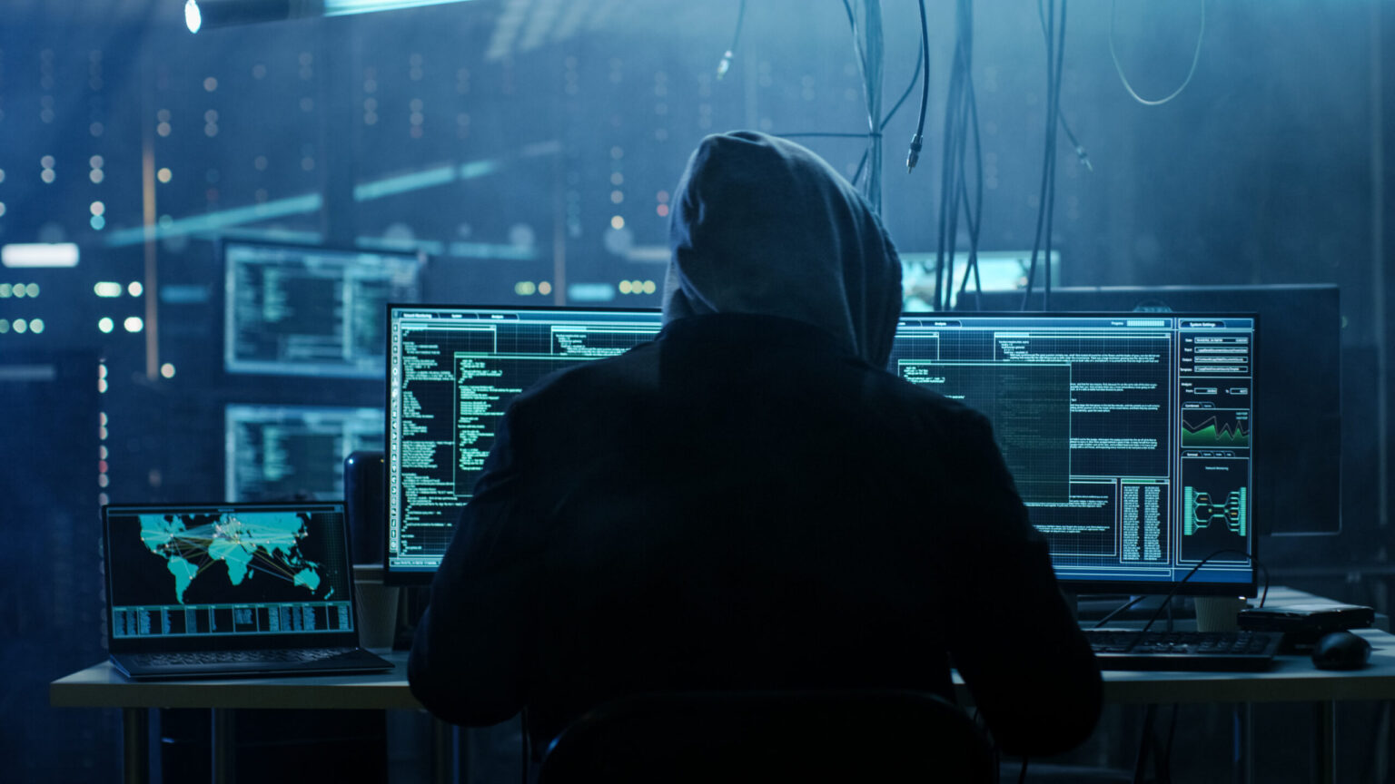 Hooded figure coding at multiple computer monitors